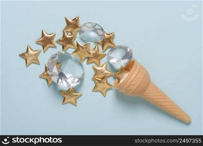 Ice cream wafer cone with shiny golden stars and gems on blue pastel background flatlay