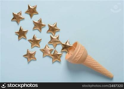 Ice cream wafer cone with shiny golden stars on blue pastel background top view