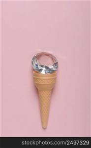 Ice cream waffle cone with shiny jewel on pink pastel background flat lay