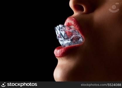 Ice cube in a woman&rsquo;s mouth against black background.