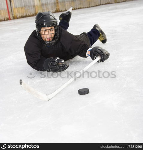 Ice hockey player boy in uniform sliding on ice holding stick out towards puck.