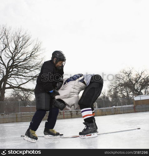 Ice hockey player boy roughing up another player on the ice rink.
