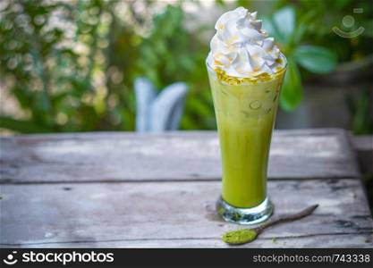 Ice Matcha green tea with whipped cream on wooden table,garden background.