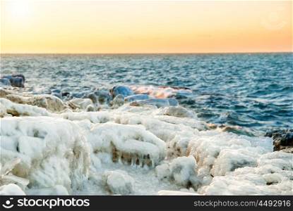 Ice on the rocks near sea with beautiful orange sunset