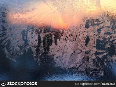 Ice patterns, water drops and sunlight on a window glass on a winter morning, close-up natural texture