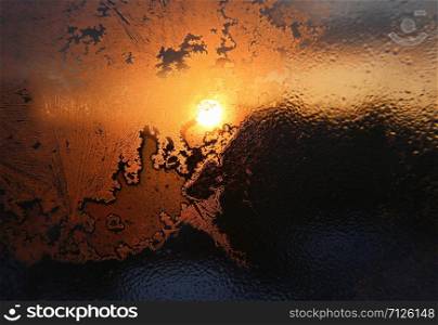 Ice patterns, water drops and sunlight on a window pane on a winter morning, close-up natural texture
