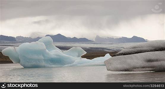 Icebergs floating in the ocean along a misty mountainous coastline