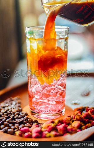 Iced americano with rose syrup and Coffee beans on wooden table in coffee cafe , background coffee