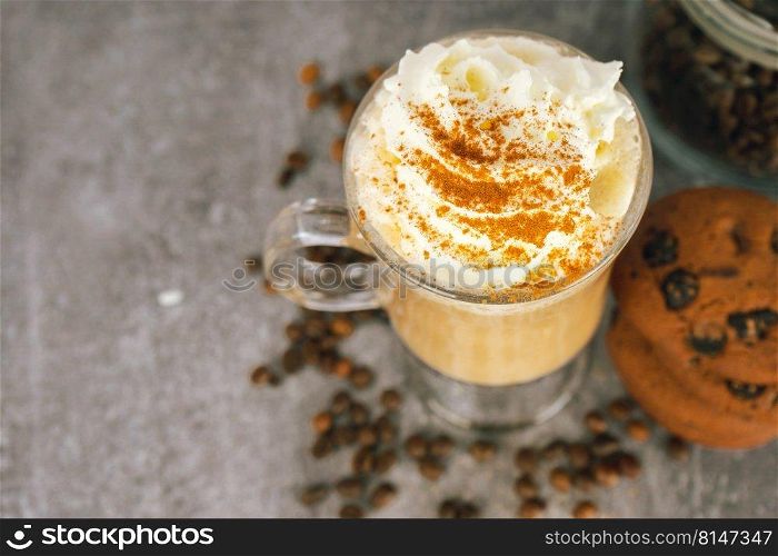 Iced caramel latte coffee in a tall glass with whipped cream on gray background with scattering of coffee beans. Top view, flat lay with copy space.. Iced caramel latte coffee in a tall glass with whipped cream.