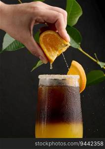 Iced coffee with orange juice in a transparent glass, a woman’s hand squeezes an orange slice into a bubble drink