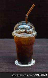 Iced coffee with straw in plastic cup. Cold coffee drink with ice on a table