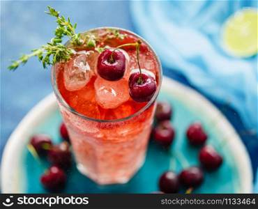 Iced organic cherry lemonade with fresh berries and thyme on the blue table