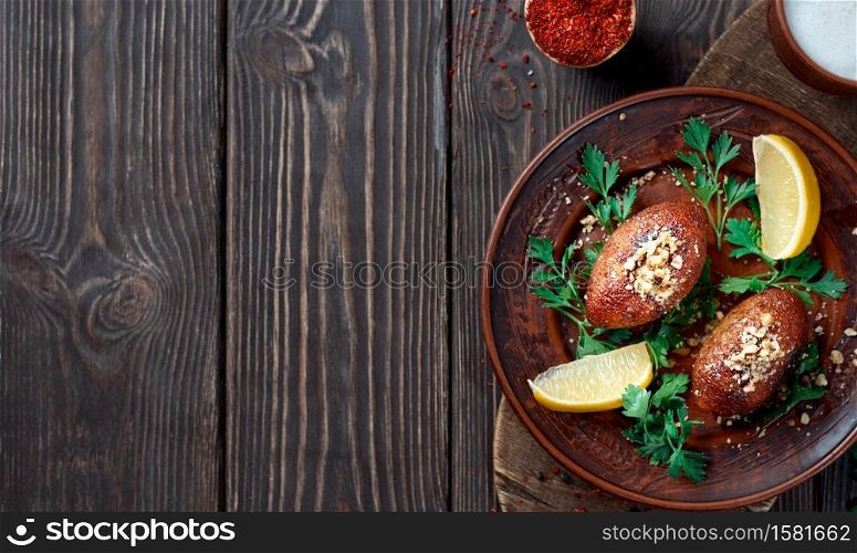Ichli kyufte (Icli kufta) cutlets or meatballs of meat in shell of bulgur, sprinkled with walnuts, hearty meat dish - cuisine Middle East. Clay plate with cilantro and lemon. Flat lay with copy space