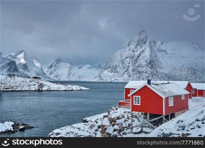 Iconic Hamnoy fishing village on Lofoten Islands, Norway with red rorbu houses. With falling snow in winter.. Hamnoy fishing village on Lofoten Islands, Norway