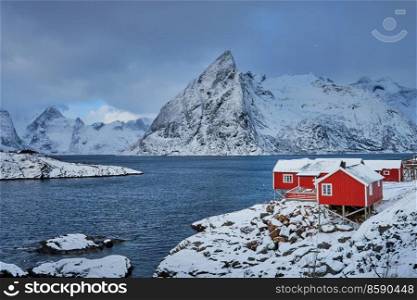 Iconic Hamnoy fishing village on Lofoten Islands, Norway with red rorbu houses. With falling snow in winter.. Hamnoy fishing village on Lofoten Islands, Norway