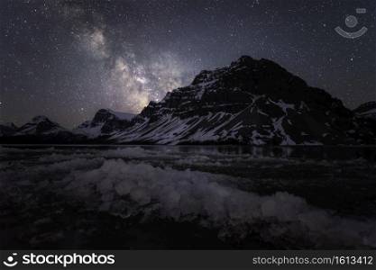 Icy blocks along the shore of Bow Lake with the Milky Way shining behind the Canadian Rockies along the Icefields Parkway in Banff National Park.