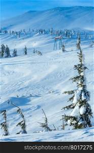 Icy snowy fir trees and ski lift on winter morning slope.