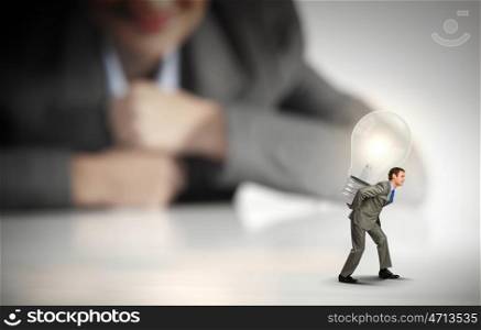 Idea concept. Businesswoman looking at miniature of man carrying light bulb on back