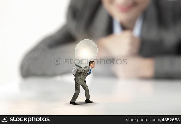 Idea concept. Businesswoman looking at miniature of man carrying light bulb on back