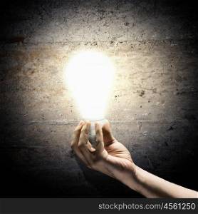 Idea concept. Close up image of human hand holding electrical bulb in darkness