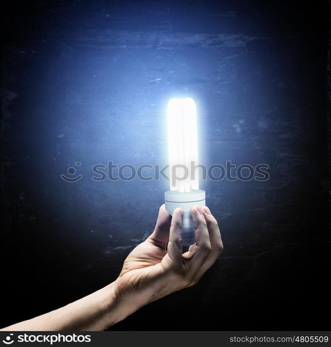 Idea concept. Close up image of human hand holding electrical bulb in darkness