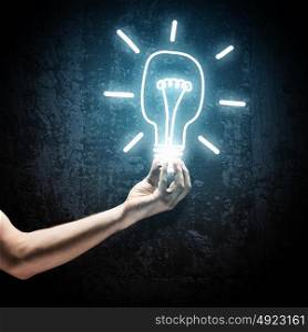 Idea concept. Close up image of human hand holding electrical bulb in darkness