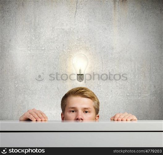 Idea concept. Half of face of young man looking out out from under the table