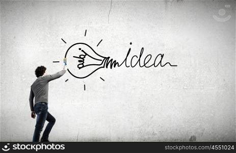 Idea concept. Young businessman standing with back and painting word idea on wall