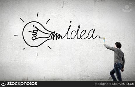 Idea concept. Young businessman standing with back and painting word idea on wall