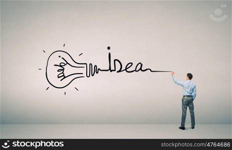 Idea concept. Young businessman standing with back and writing word idea on wall