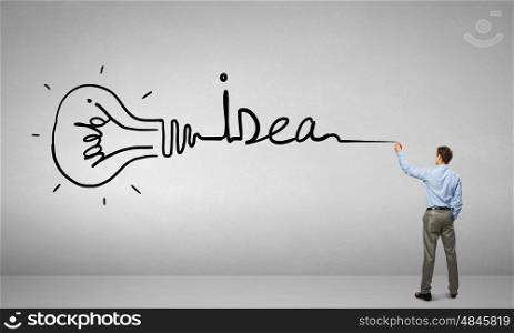 Idea concept. Young businessman standing with back and writing word idea on wall