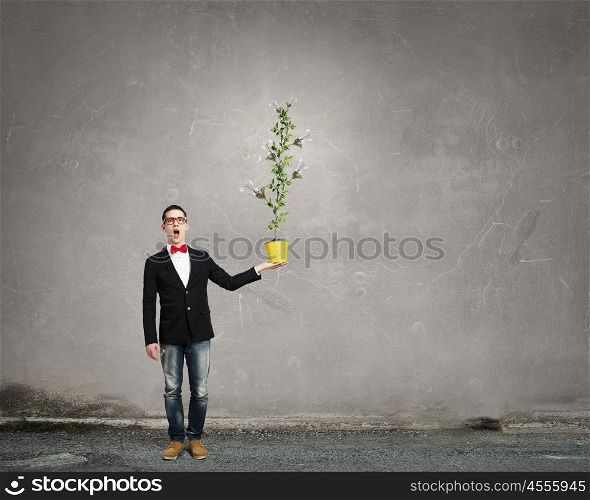Idea for progressive growth. Young man wearing jacket holding yellow bucket with green plant