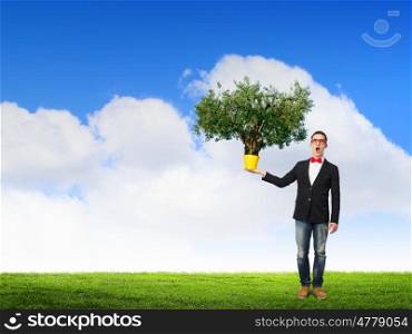 Idea for progressive growth. Young man wearing jacket holding yellow bucket with green plant