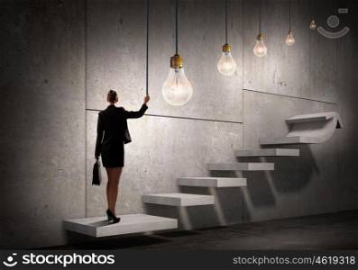 Idea for successful progress and promotion. Back view of businesswoman standing on ladder and big idea bulb