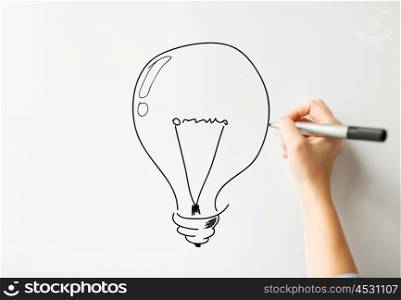idea, inspiration, business, people and education concept - close up of hand with marker drawing light bulb on white board or wall