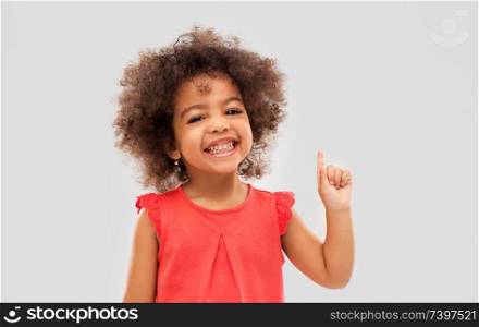 idea, warning and childhood concept - happy little african american girl pointing finger up over grey background. little african american girl pointing finger up