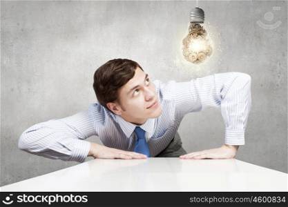 Ideas of work structuring. Businessman leaning on table and looking at bulb with gears