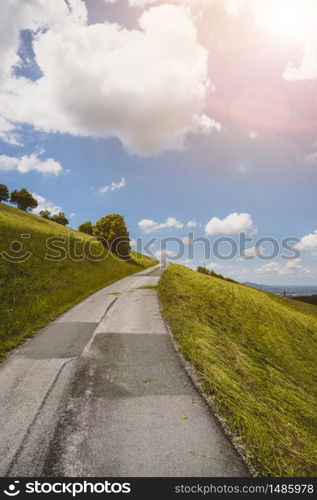 Idyllic mountain landscape, steep asphalted mountain road, green meadow and blue sky with clouds