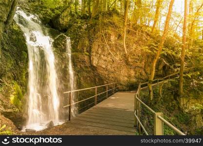 Idyllic scenery of a small waterfall and a bridge that crosses it, in the forests of the Swiss Alps from Walensee, St Gallen Canton, Switzerland.