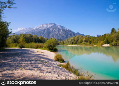 Idyllic shore landscape: Blue clear water, flowers, pebble beach and mountains