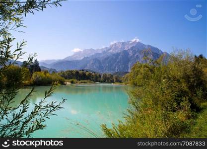 Idyllic shore landscape: Blue clear water, flowers, pebble beach and mountains