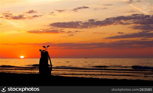 Idyllic shot of sunset by the sea waters, warm, orange and red colors and bag with golf club equipment. Idyllic shot of sunset and golf clubs