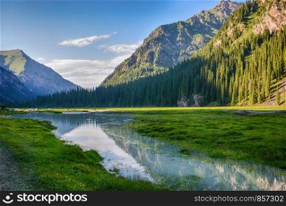 Idyllic summer landscape with hiking trail in the mountains with beautiful fresh green mountain pastures, river with reflection and forest. Terskey Alatoo mountains, Tian-Shan, Karakol, Kyrgyzstan