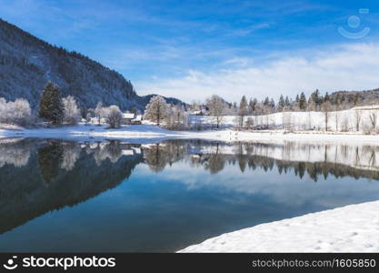 Idyllic winter landscape  Reflection lake, house and snowy trees and mountains