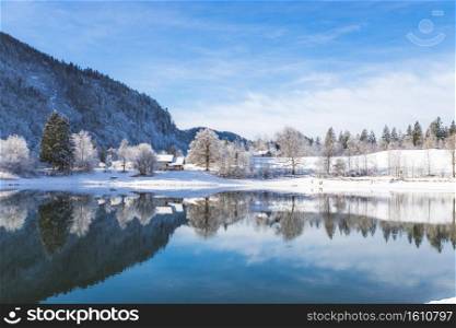 Idyllic winter landscape  Reflection lake, house and snowy trees and mountains
