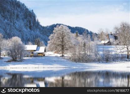 Idyllic winter landscape  Reflection lake, house and snowy trees and mountains