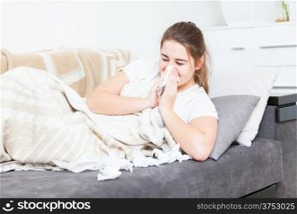 Ill woman lying in bed and sneezing in paper tissue