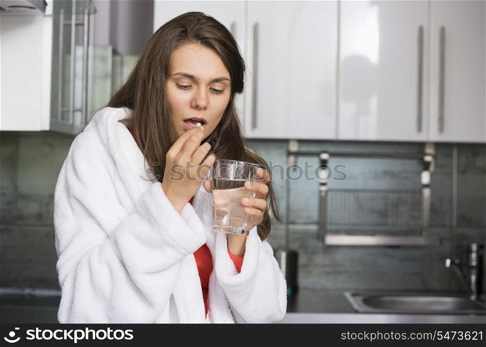 Ill woman taking medicine in kitchen