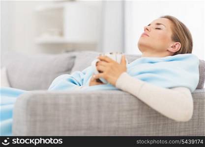 Ill woman with cup of hot beverage sitting on couch