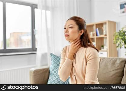 illness and health problem concept - sick asian woman touching her sore throat at home. sick asian woman touching her sore throat at home
